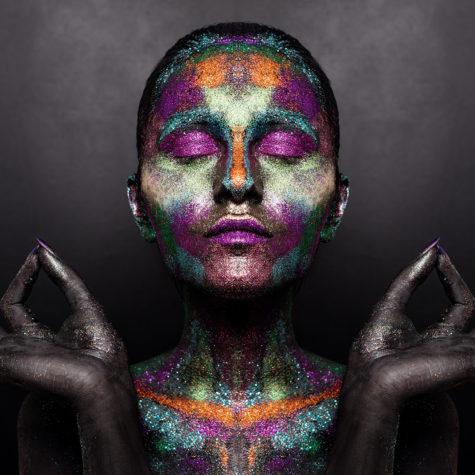 Young artistic woman in black paint and colourful powder. Glowing dark makeup. Creative body art on the theme of space and stars. Bodypainting project: art, beauty, fashion